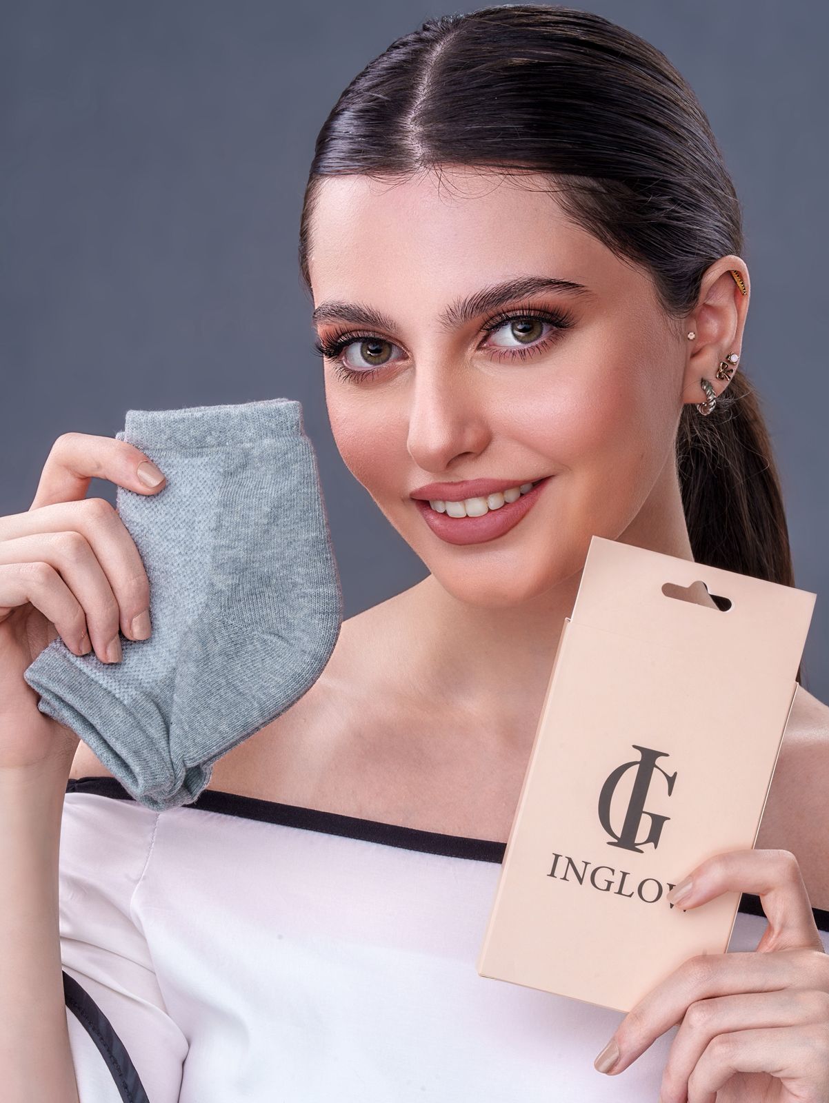 Woman holding a pair of gray socks and a beige card with 'INGLIO' branding against a dark background