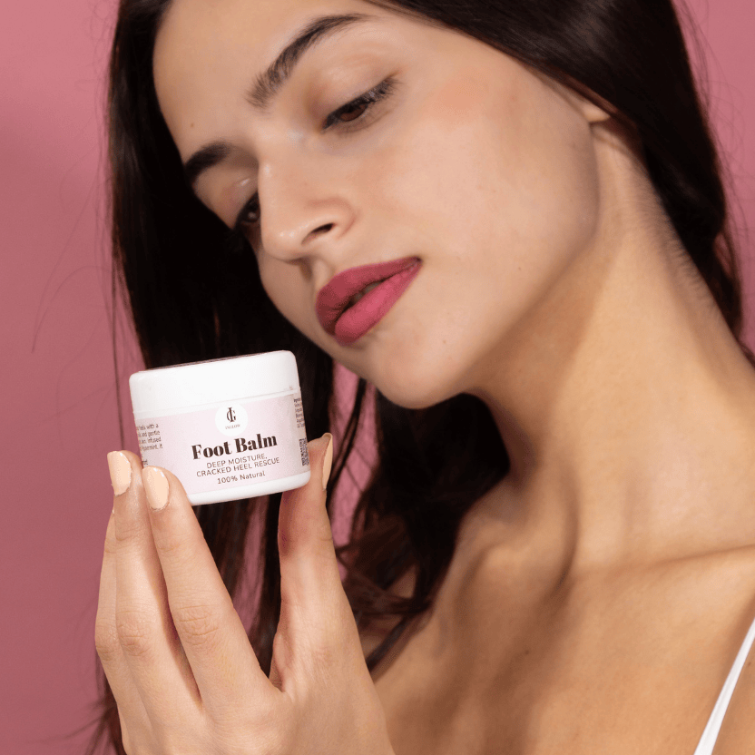 Woman holding a jar of foot balm against a pink background